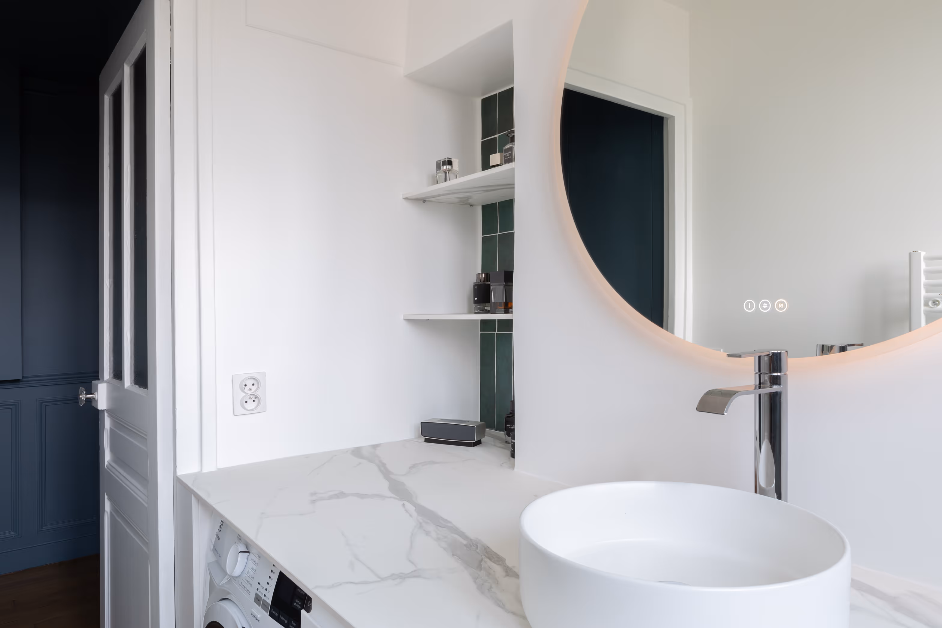 Rénovation de salle de bain d'appartement haussmannien à Paris 12 : vasque ronde, miroir lumineux, étagères encastrées et carrelage vert foncé.